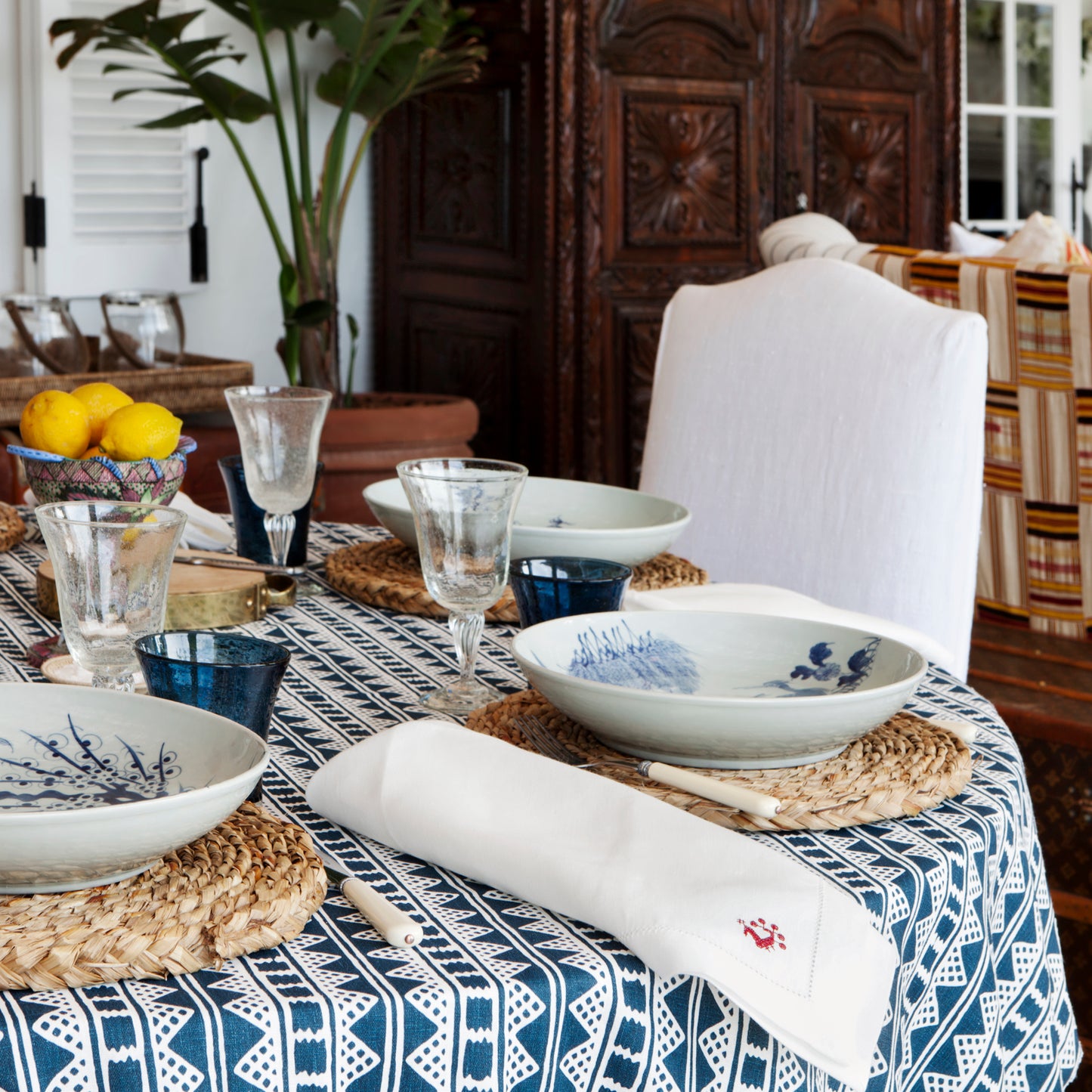 Dining table set with blue and white dishes, glasses, and a patterned tablecloth.