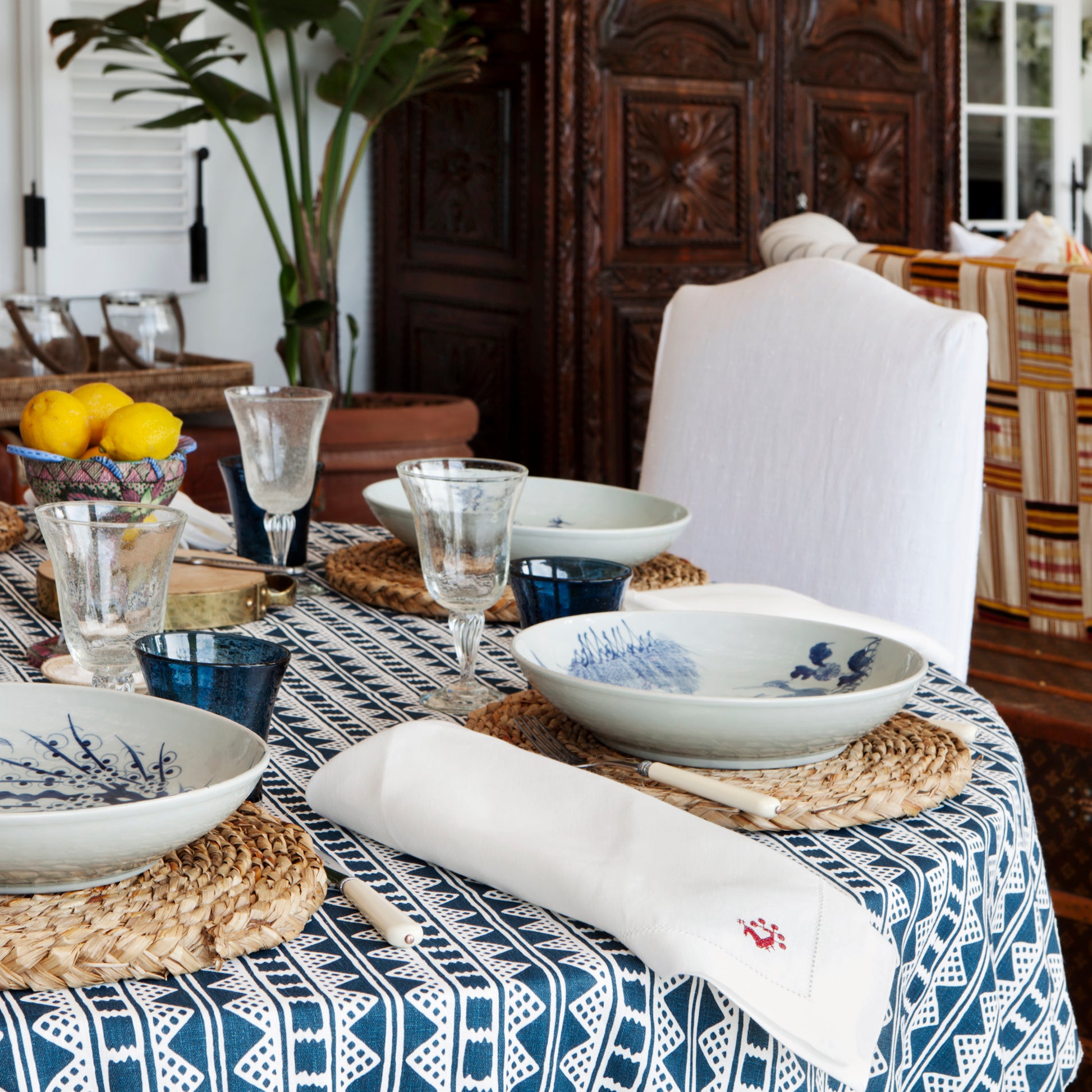 Dining table set with blue and white dishes, glasses, and a patterned tablecloth.