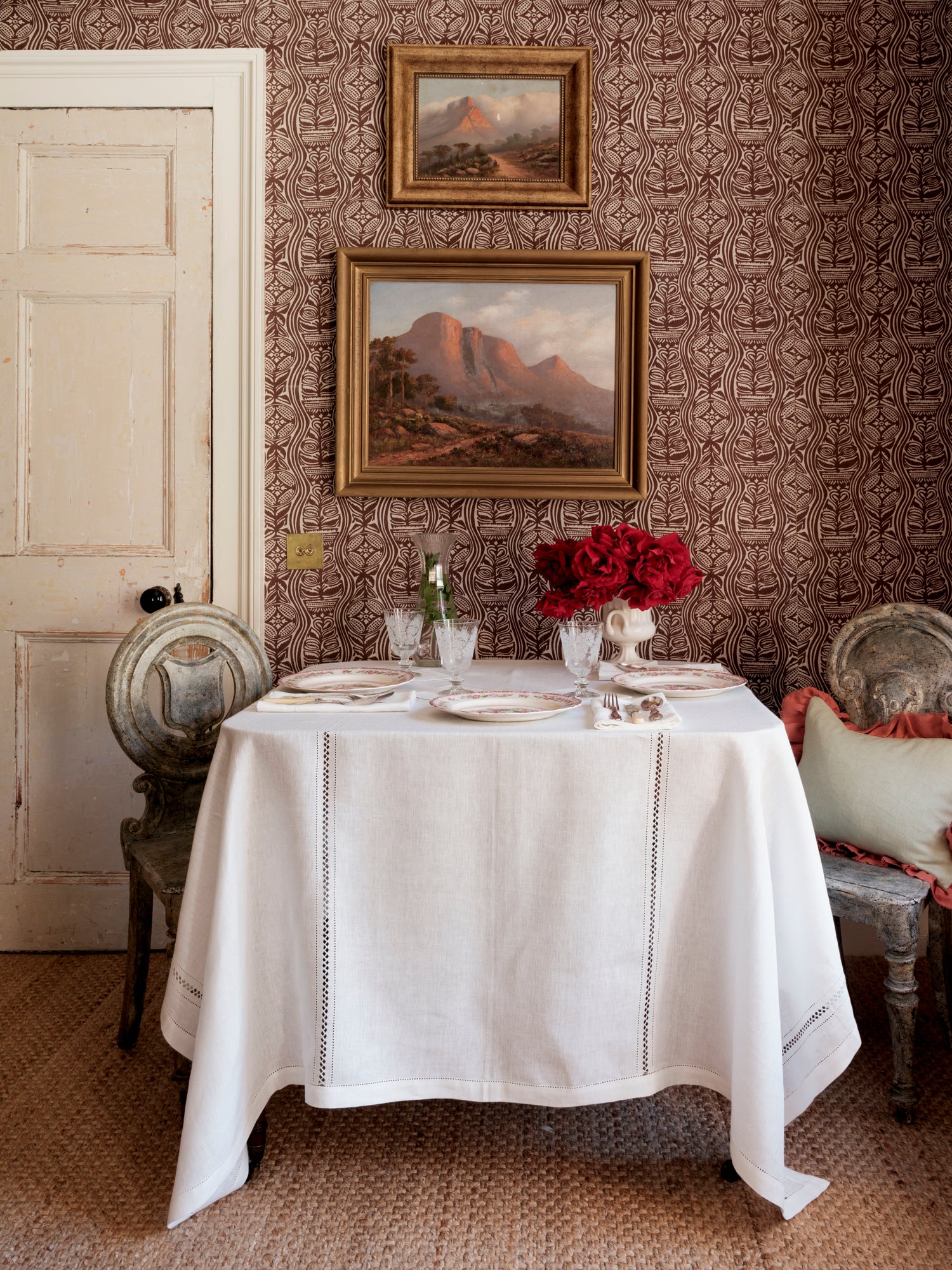 Dining room with a table set for a meal, featuring white tablecloth, red flowers, and framed artwork on the wall.